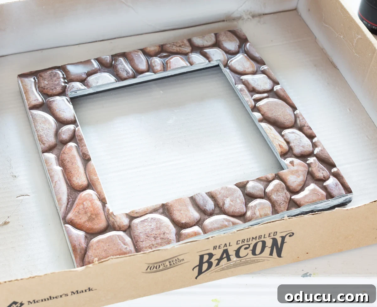 Applying an adhesive faux stone tile from the Dollar Tree onto a picture frame, highlighting the adhesion process.