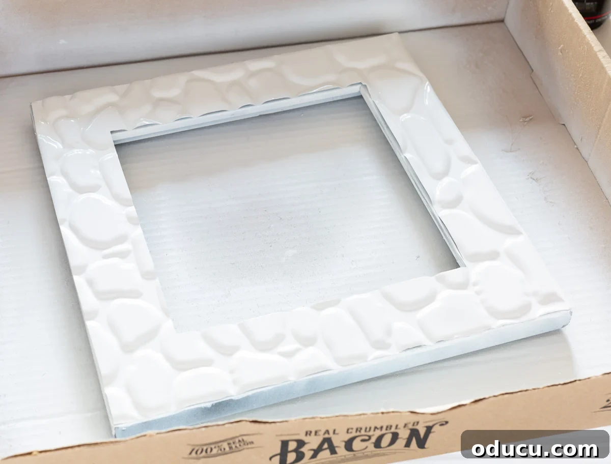 A faux adhesive tile being spray painted inside a spray painting box, demonstrating the painting technique.