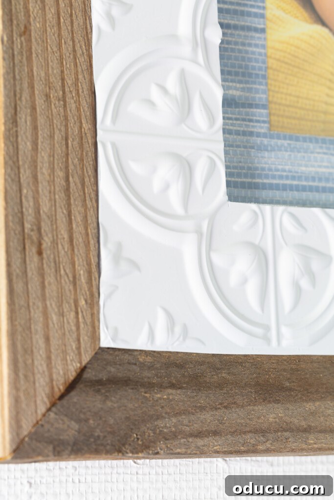 Close up of a thrifted frame with added wood, vintage tin adhesive tile, and wallpaper scraps, showcasing the intricate texture and craftsmanship.