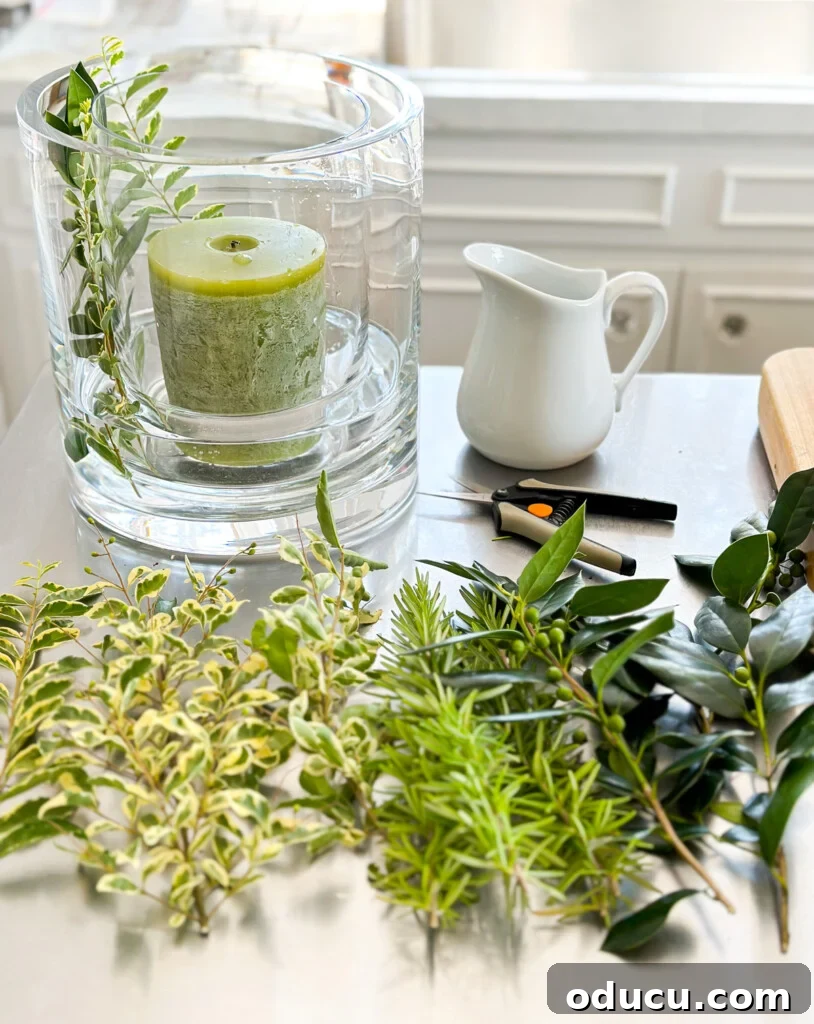 Effortless Greenery Candle Vases 4 All materials required for making a DIY glass candle vase, including two vases, clippings, clippers, a candle, and water, laid out on a surface.