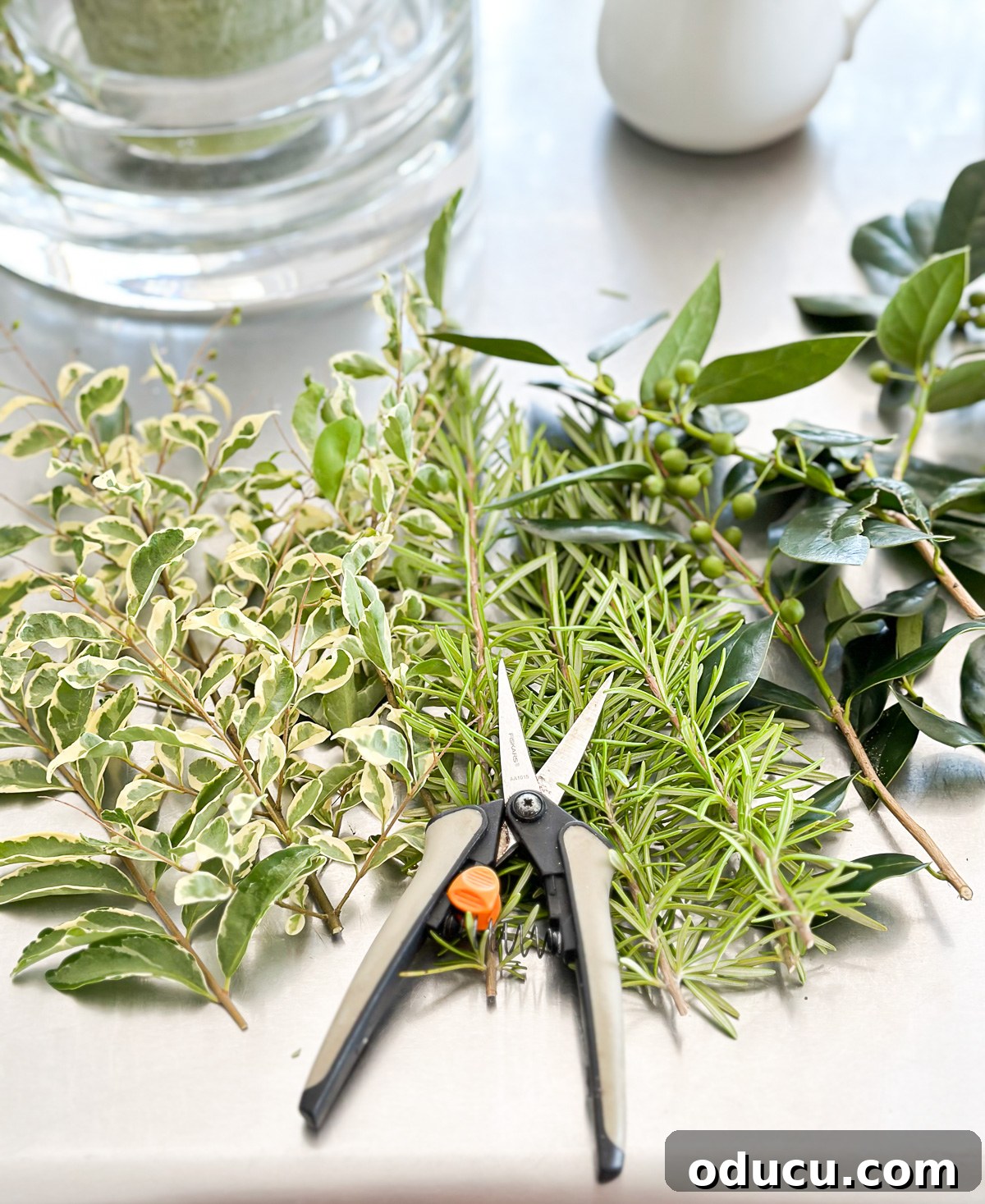 A collection of fresh herbs and shrub clippings, gathered from a garden, intended for a DIY summer table centerpiece candle vase.