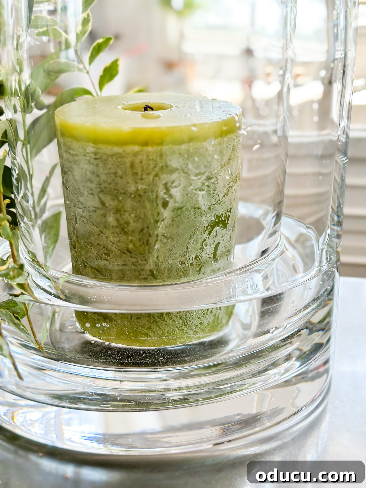 Illustrates a smaller cylinder glass vase placed inside a larger one, with water added to the larger vase and a pillar candle placed in the smaller vase.