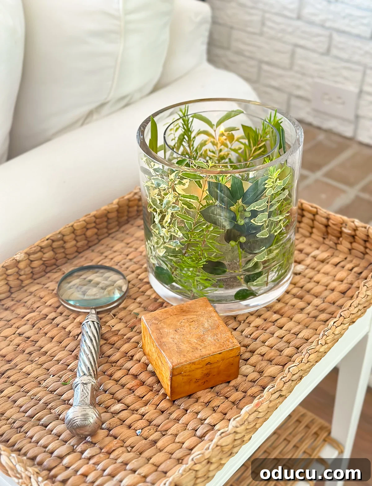 A completed summer table decor piece featuring two glass vases, fresh herbs, and shrub cuttings from a yard, beautifully displayed on a table.