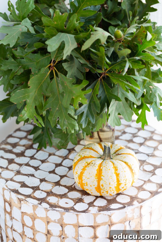 Creating a Cozy Fall Living Room Sanctuary 16 Mini tiger pumpkin on accent table with vase full of green leaves next to it.