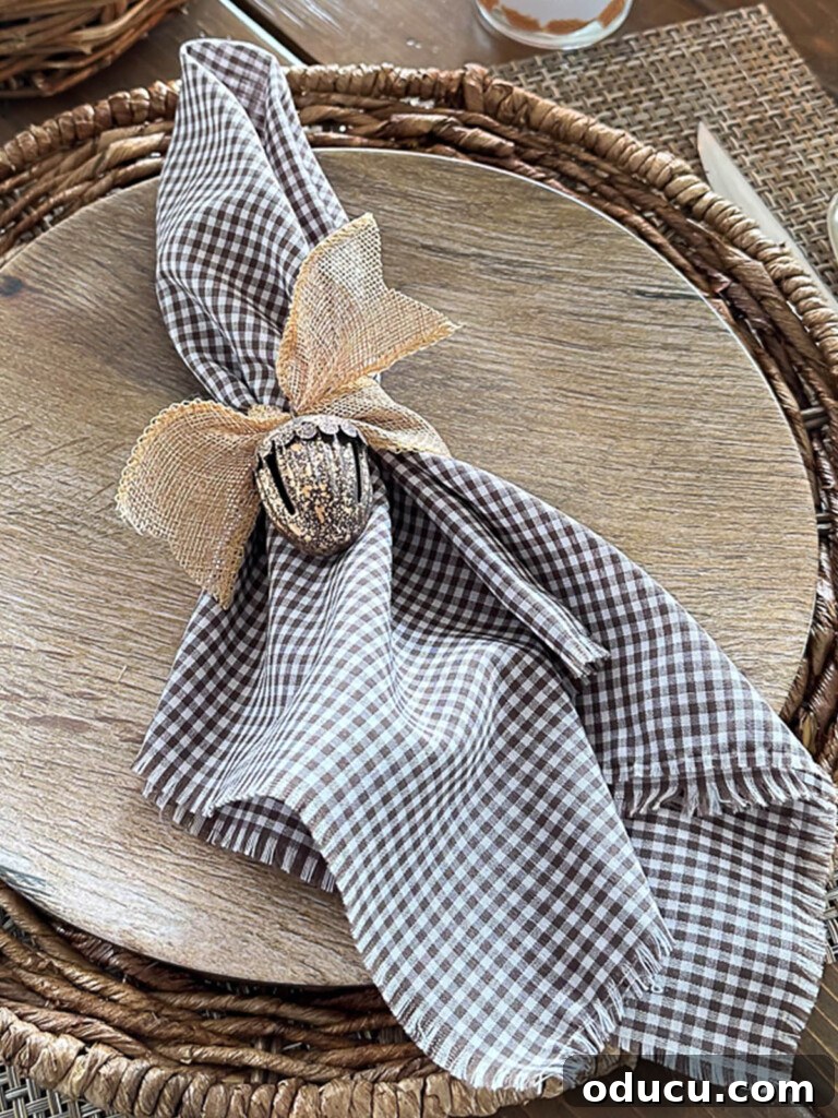 Simple & Stunning Thanksgiving Table Settings 14 Brown and white gingham napkin tied with burlap ribbon and a metal acorn jingle bell on a wood look dinner plate