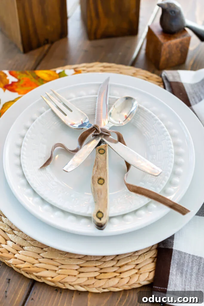Simple & Stunning Thanksgiving Table Settings 16 Table place setting of a white dinner plate layered with a fork, knife and spoon tied with brown ribbon