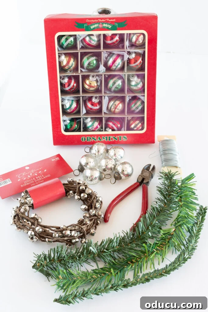 Simple Steps to Gorgeous Christmas Taper Candle Rings 4 Crafting supplies laid out for DIY Christmas candle rings: mini Shiny Brite ornaments, faux evergreen garland ties, festive jingle bells, and wire cutters.