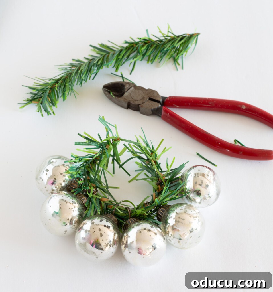 Simple Steps to Gorgeous Christmas Taper Candle Rings 5 Step-by-step guide showing how to thread small, colorful Christmas ornaments onto a flexible garland tie to create a custom candle ring.