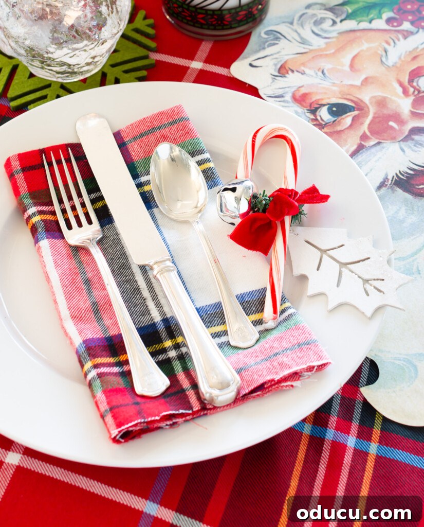 Joyful and Merry Christmas Dinner Table 8 Christmas table setting with a festive red and white plaid theme, Santa accents, a candy cane, and a jingle bell on each dinner plate for decoration.