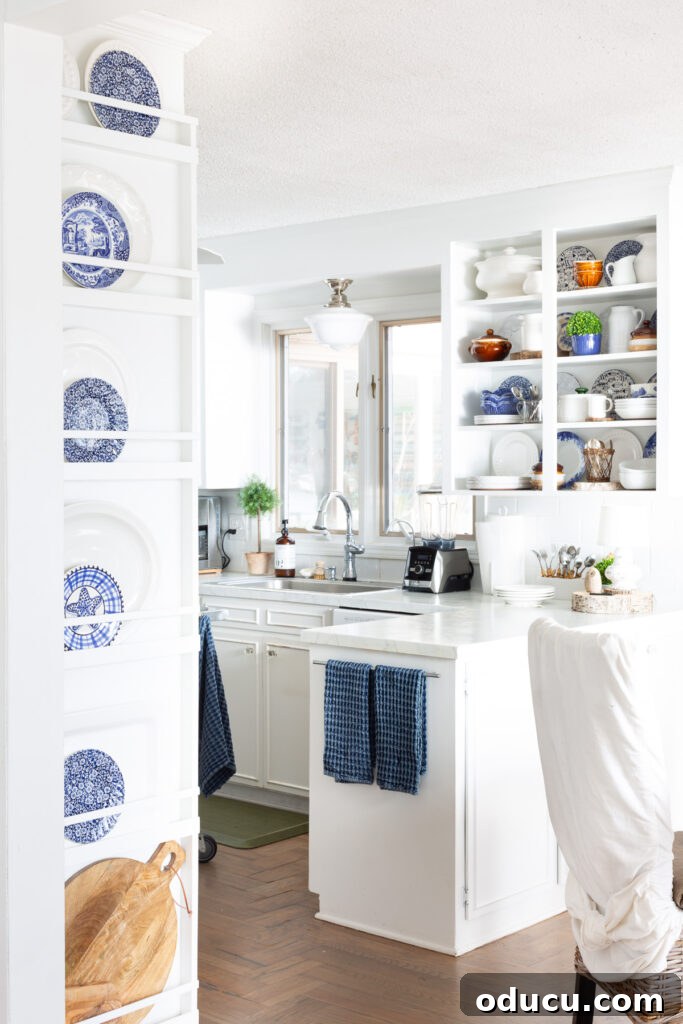 Effortless Winter Decor 9 Bright white kitchen featuring thoughtful blue accents, including plates on a wall rack and blue dish towels, creating a fresh and cohesive look.