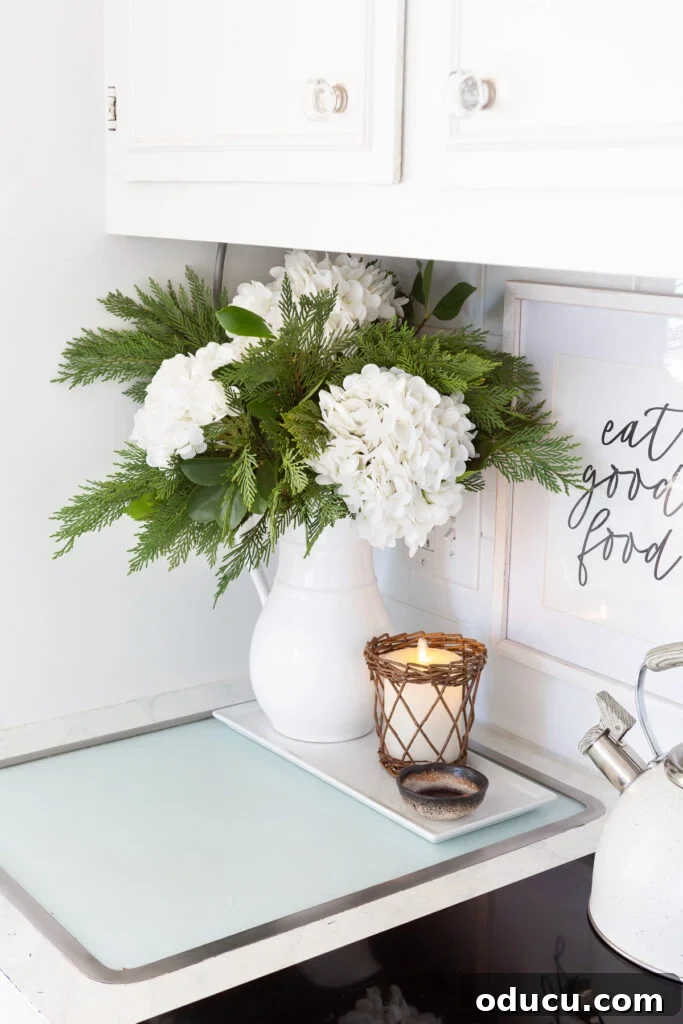 Cheery winter decor featuring large white hydrangeas and greenery mixed in a white pitcher, perfect for a winter white floral arrangement.