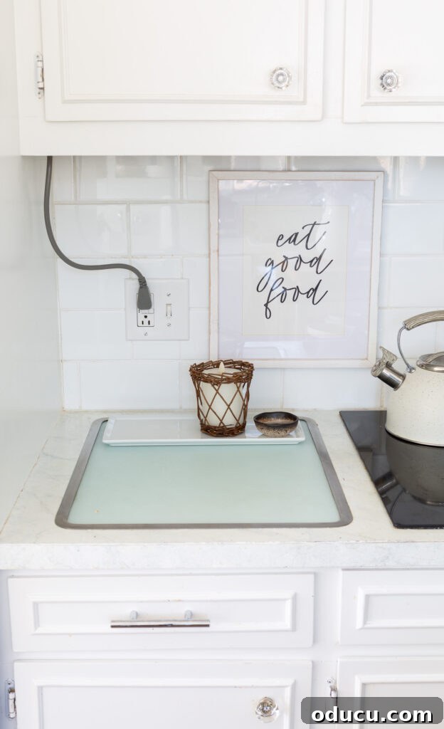 An exposed electrical cord running down from upper cabinets to an outlet on a kitchen backsplash, the secret this winter white floral arrangement hides.