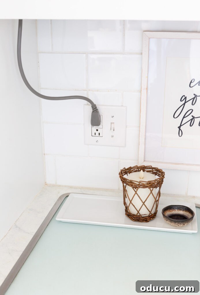 The unsightly electrical cord coming from the upper cabinet to the kitchen counter, discreetly hidden by a winter white floral arrangement.
