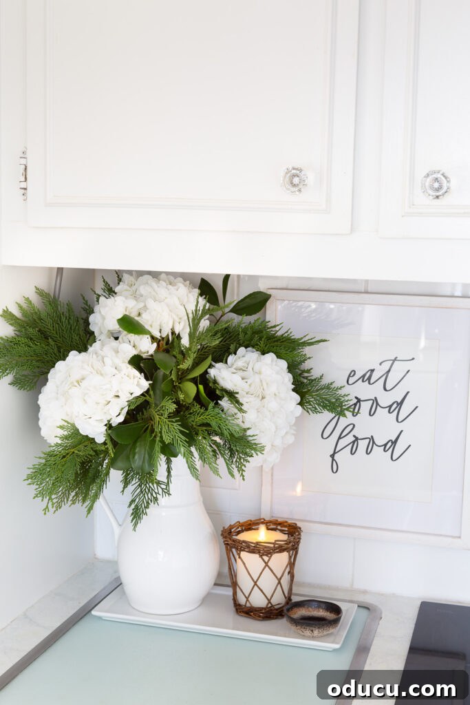 Cheery winter decor featuring large white hydrangeas and greenery mixed in a white pitcher, perfect for a winter white floral arrangement.