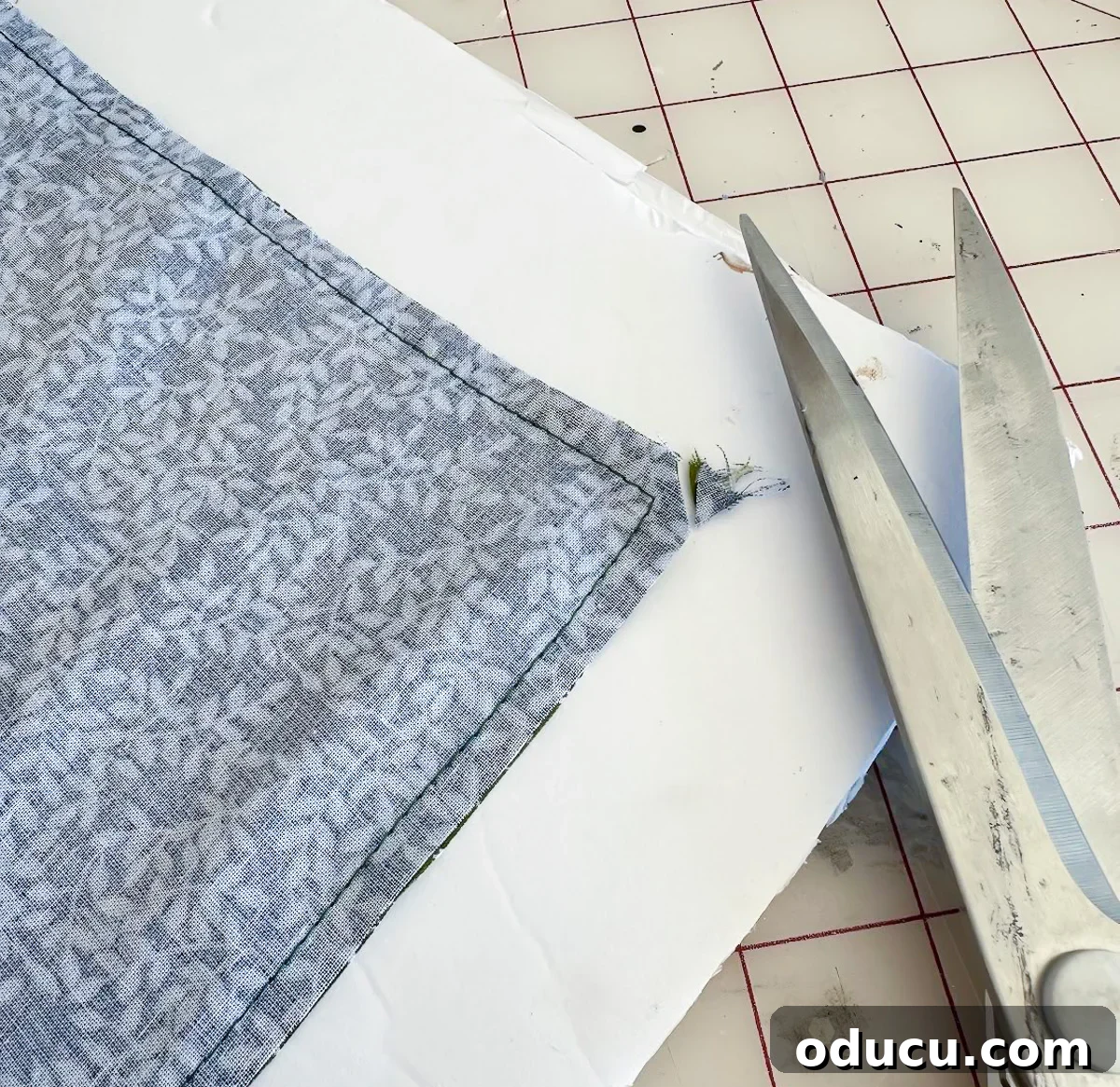 Snipping the corner of sewn fabric with scissors, demonstrating a technique to achieve crisp, sharp corners for a finished napkin.