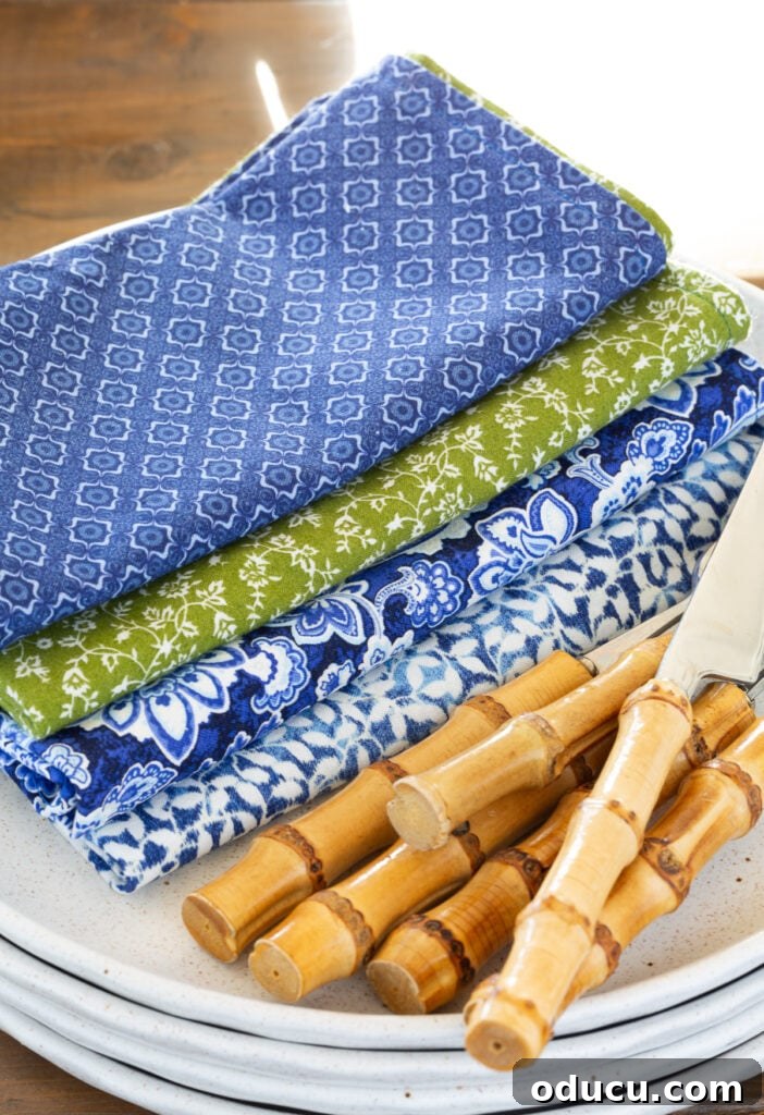 Whip Up Wonderful Napkins: A Simple Guide to Colorful Table Decor 5 4 blue, white, and green patterned cloth napkins folded on plates with bamboo utensils, showcasing a mix-and-match aesthetic.