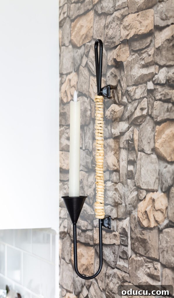 Decorate Wisely Reap the Rewards 11 Black metal and natural cord wrapped candle sconce hanging on a wall with stacked stone wallpaper.