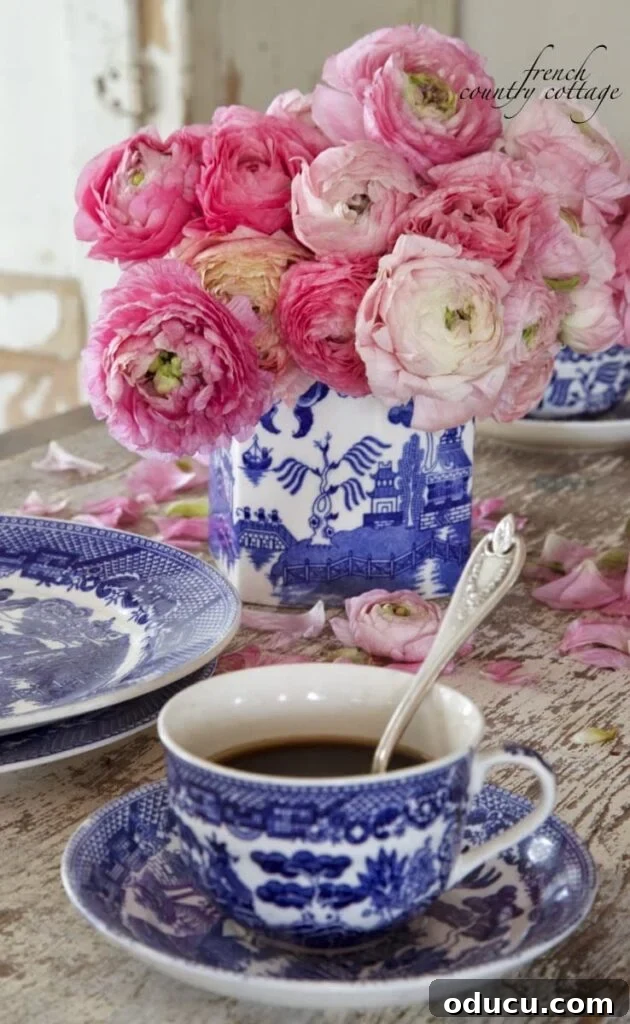 Trend Tracker: Volume 184 2 Beautiful roses in a blue and white vase next to a coffee cup on a rustic table, evoking French Country Cottage style.