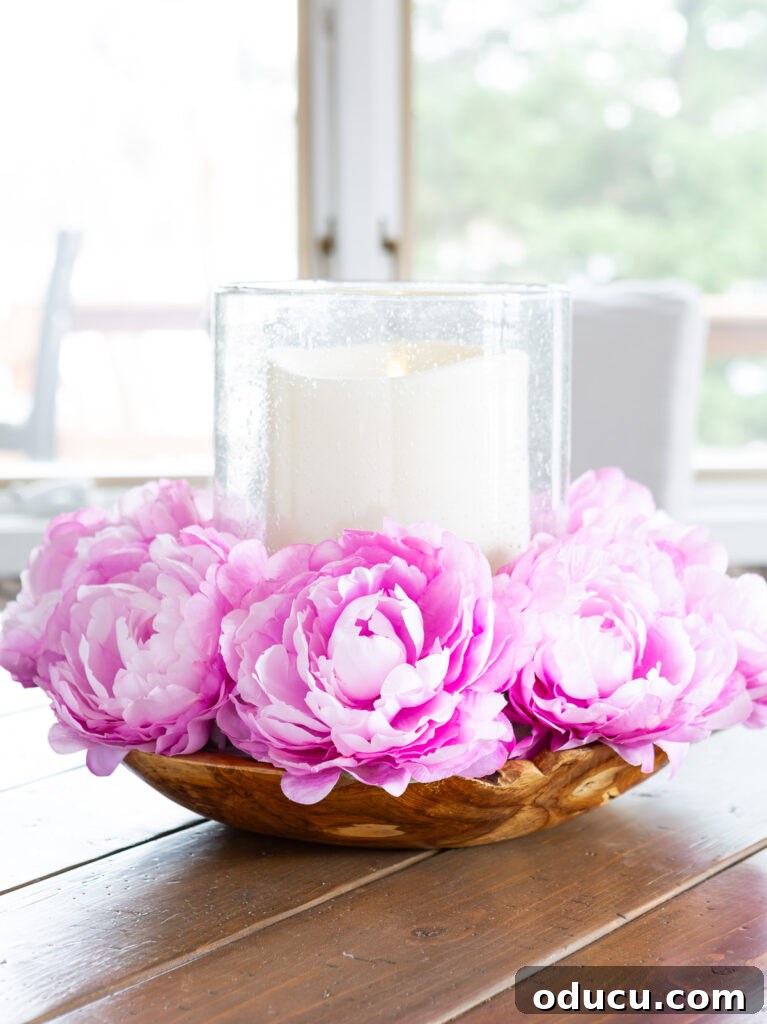 Effortless Easter Table Decor and Centerpiece Ideas 11 Pink faux flowers surrounding a large candle, artfully arranged in a rustic bowl on a wooden surface, highlighting a simple yet elegant spring table centerpiece.