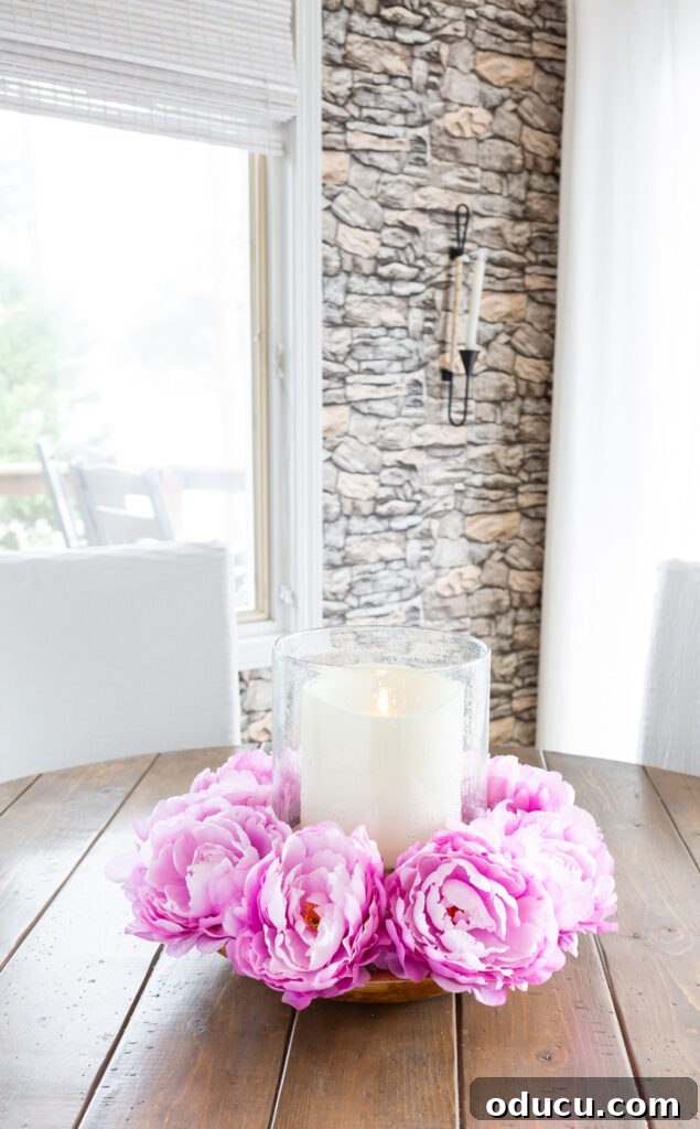 Effortless Easter Table Decor and Centerpiece Ideas 9 Elegant pink floral table centerpiece featuring a large candle, set on a rustic wood table, creating a warm and inviting atmosphere.