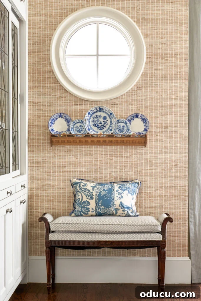 Style Quest 187 2 Edmondson-Ave-designer-Sara-Johnson decorated corner of a room with blue and white plates against beige woven wallpaper, featuring a chic armchair and elegant side table.