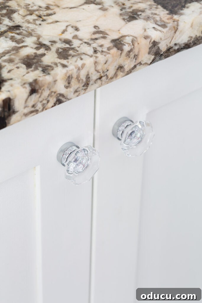 Primary Bathroom Sanctuary Unveiled 19 glass and polished chrome cabinet knobs on white bathroom cabinets.