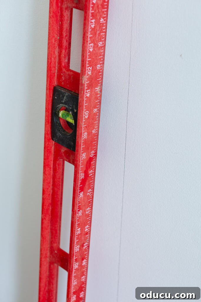 Walls of Welcome 12 A vibrant red bubble level being meticulously used to draw a perfectly straight vertical line on a wall, marking the precise placement for the first panel of wallpaper, ensuring a level and professional installation.