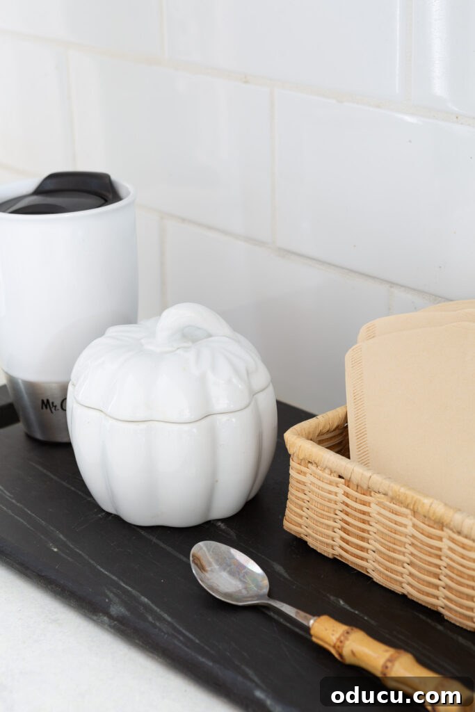 Hold Off on Fall Decorating Try This Alternative 13 white ceramic pumpkin bowl with lid to hold sugar for the fall season placed on a kitchen counter coffee station.