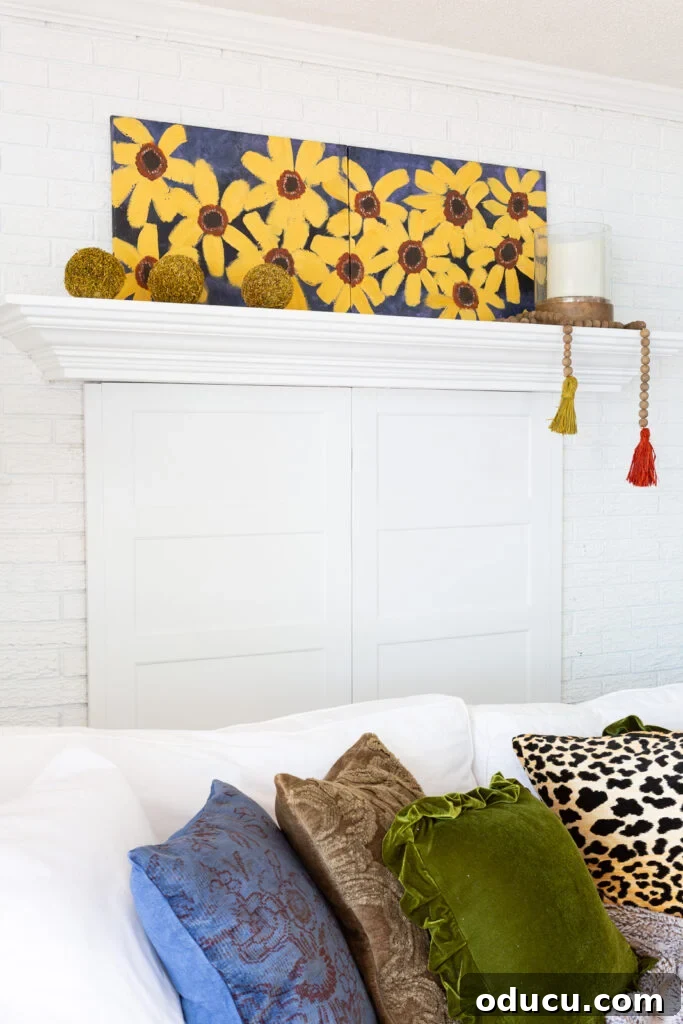 Cozy Autumn Vibes: Living Room Refresh 9 Side view of painted fall flower canvas on a mantel above a white sofa with fall colored and textured throw pillows.