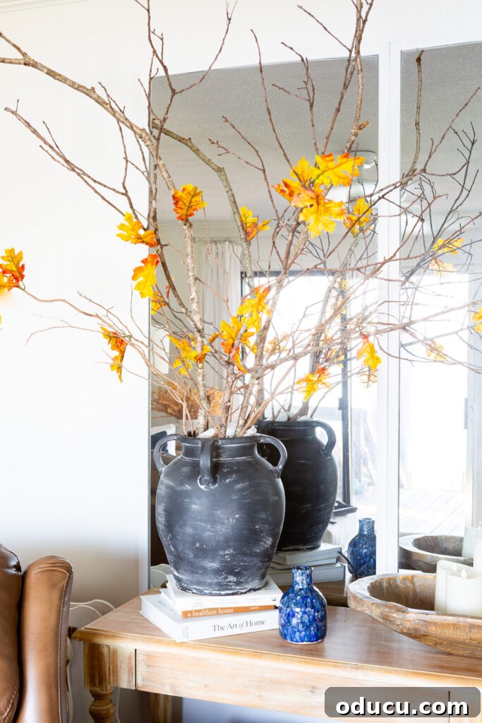 Cozy Autumn Vibes: Living Room Refresh 10 Faux fall leaves on bare tree branches in a large black vase on a console table.