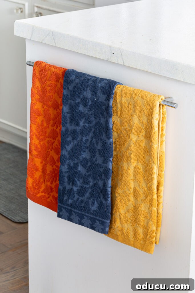 Fall Kitchen Shelves Get a Wallpaper Makeover 5 3 fall colored dish towels hanging on a towel bar in a white kitchen.