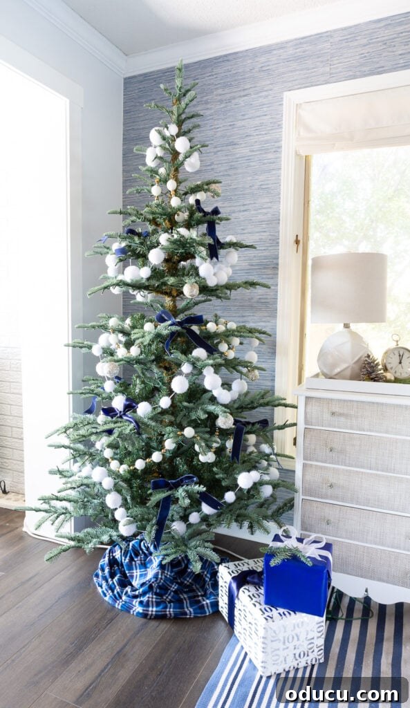 The King of My Christmas 11 7' King Noble Fir Artificial Christmas Tree with 500 Warm White LED Lights decorated with white snowball garland and blue ribbon bows.