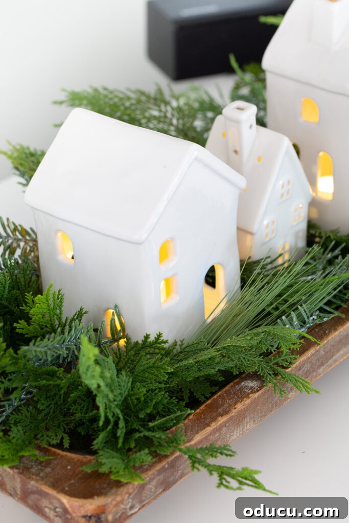 Tealight Village Magic: Fall and Holiday Decor 11 A stunning Christmas tabletop display showcasing white ceramic houses arranged in a dough bowl, beautifully accented with lush greenery.