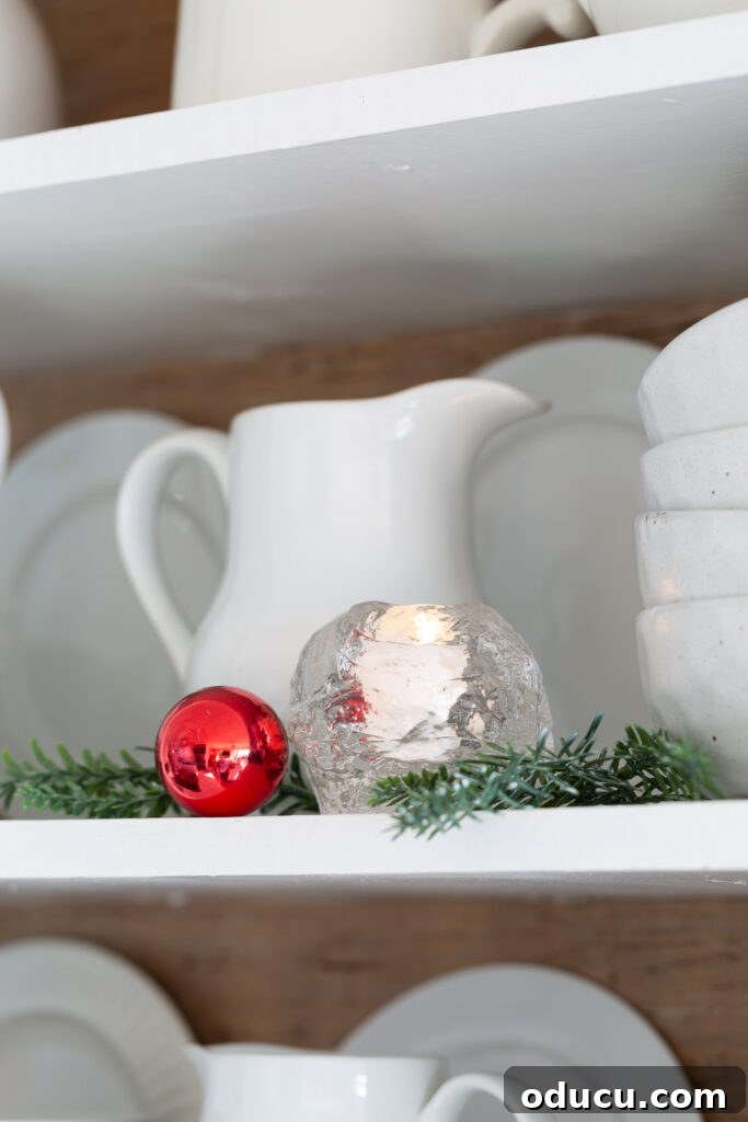 Decking the Halls for the Holidays 13 White pitcher with greenery and red Christmas ornament open shelves in kitchen.