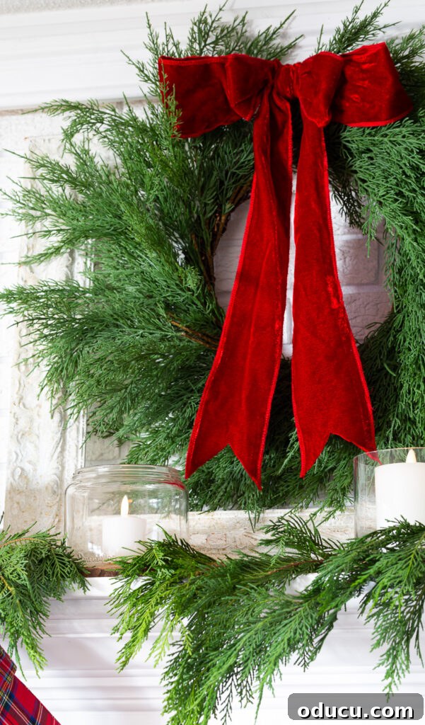 Decking the Halls for the Holidays 18 Wreath with red velvet ribbon hanging on a wall above a fireplace mantel.