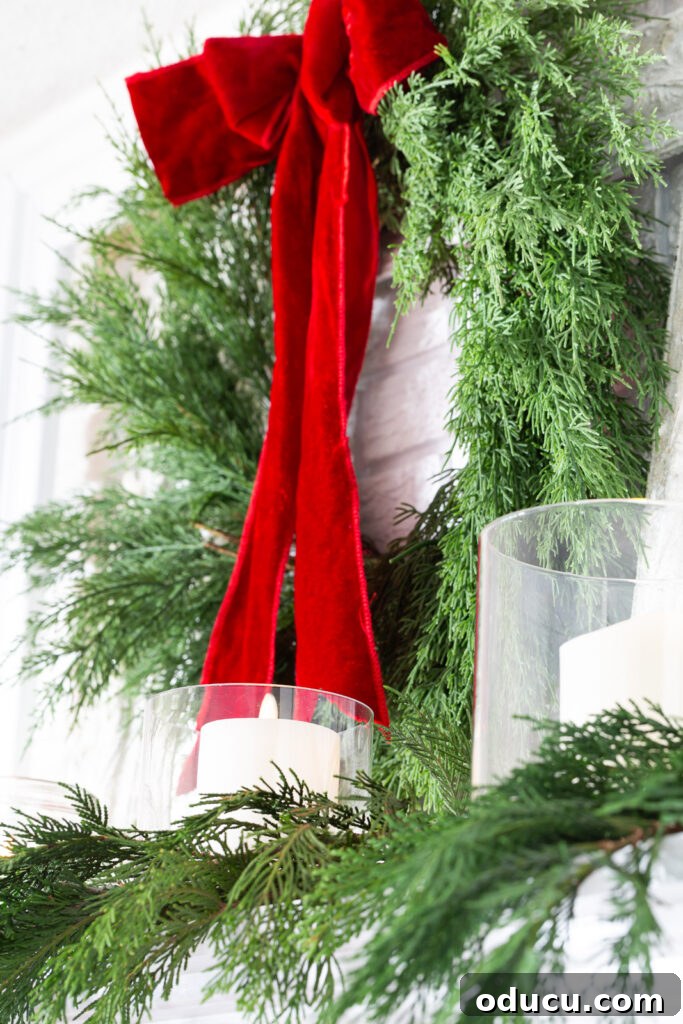 Decking the Halls for the Holidays 8 Wreath with red velvet ribbon hanging on a wall above a fireplace mantel.