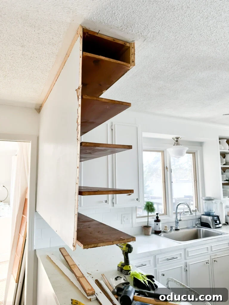 My Kitchen's Stunning Spacious Makeover 7 Side view of kitchen after partial removal of upper cabinets, revealing exposed wall and ceiling structure.