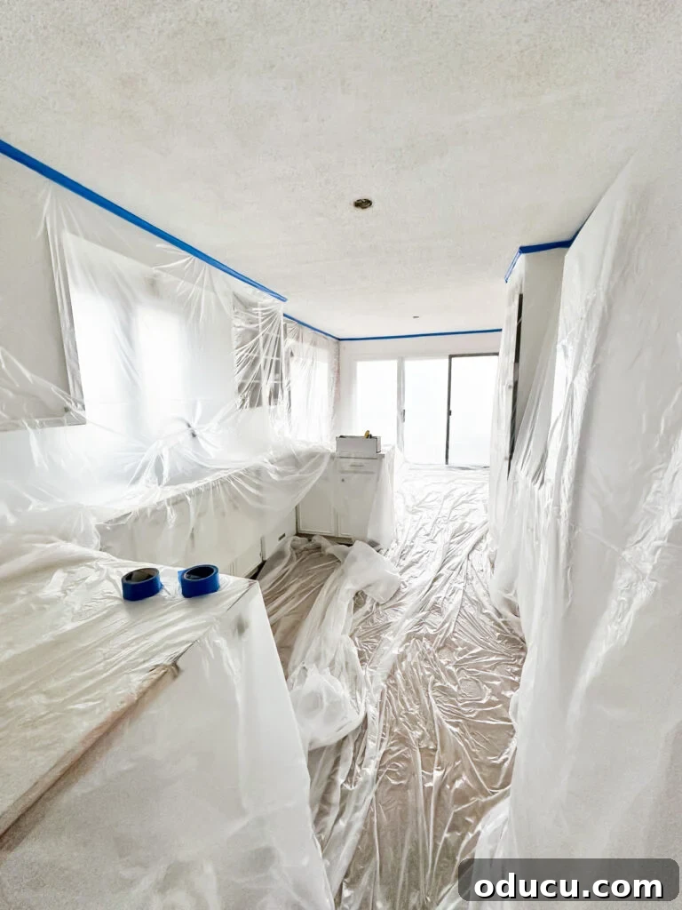 My Kitchen's Stunning Spacious Makeover 9 Kitchen prepared for popcorn ceiling removal: cabinets and floor meticulously masked with plastic sheeting to protect from dust.