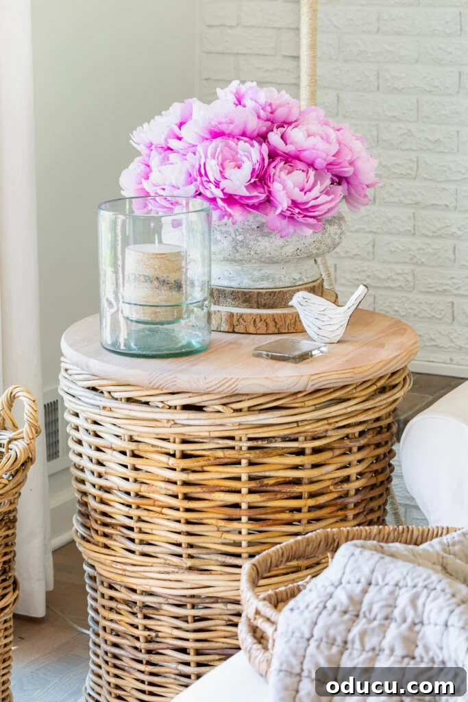 Corner of living room with a rounf wicker basket table with a faux concrete planter filled with faux peonies for early spring decor.