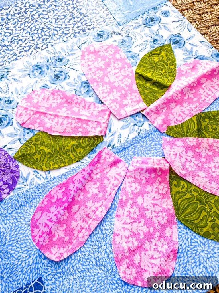 Placing cut out flower petal shapes on fabric strip covered canvas to find appealing layout.